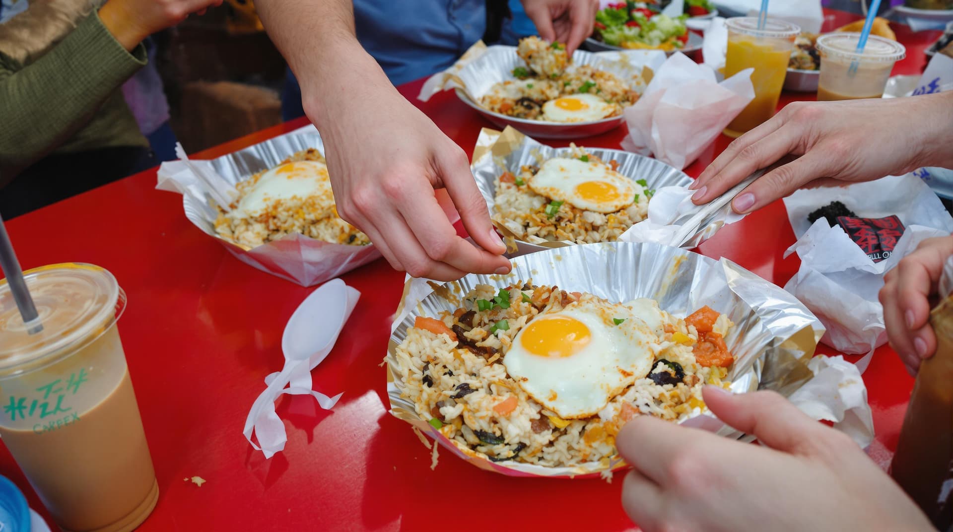 AI generated: Asian street food, fried rice with egg, red table, hands passing plates, bubble tea, takeout contain...