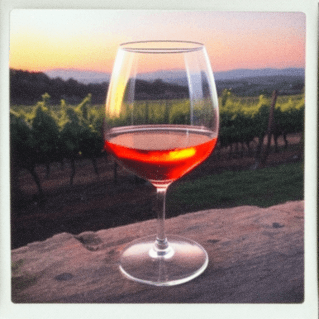 AI generated: In the foreground, close-up a single glass of wine is placed on a smooth rock, in the background a v...