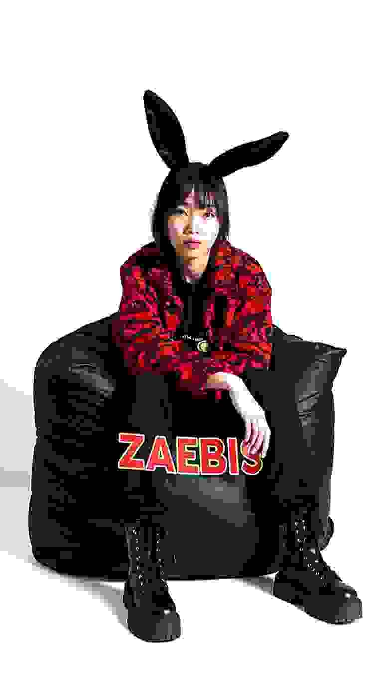 AI generated: The image shows a person sitting on top of a black bean bag chair. The person is wearing a red and b...