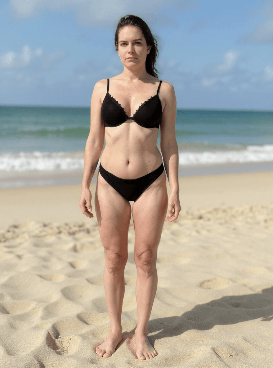 AI generated: a 25 year old is standing on a beach in a skimpy black string bikini.  Large breasts with cleavage s...