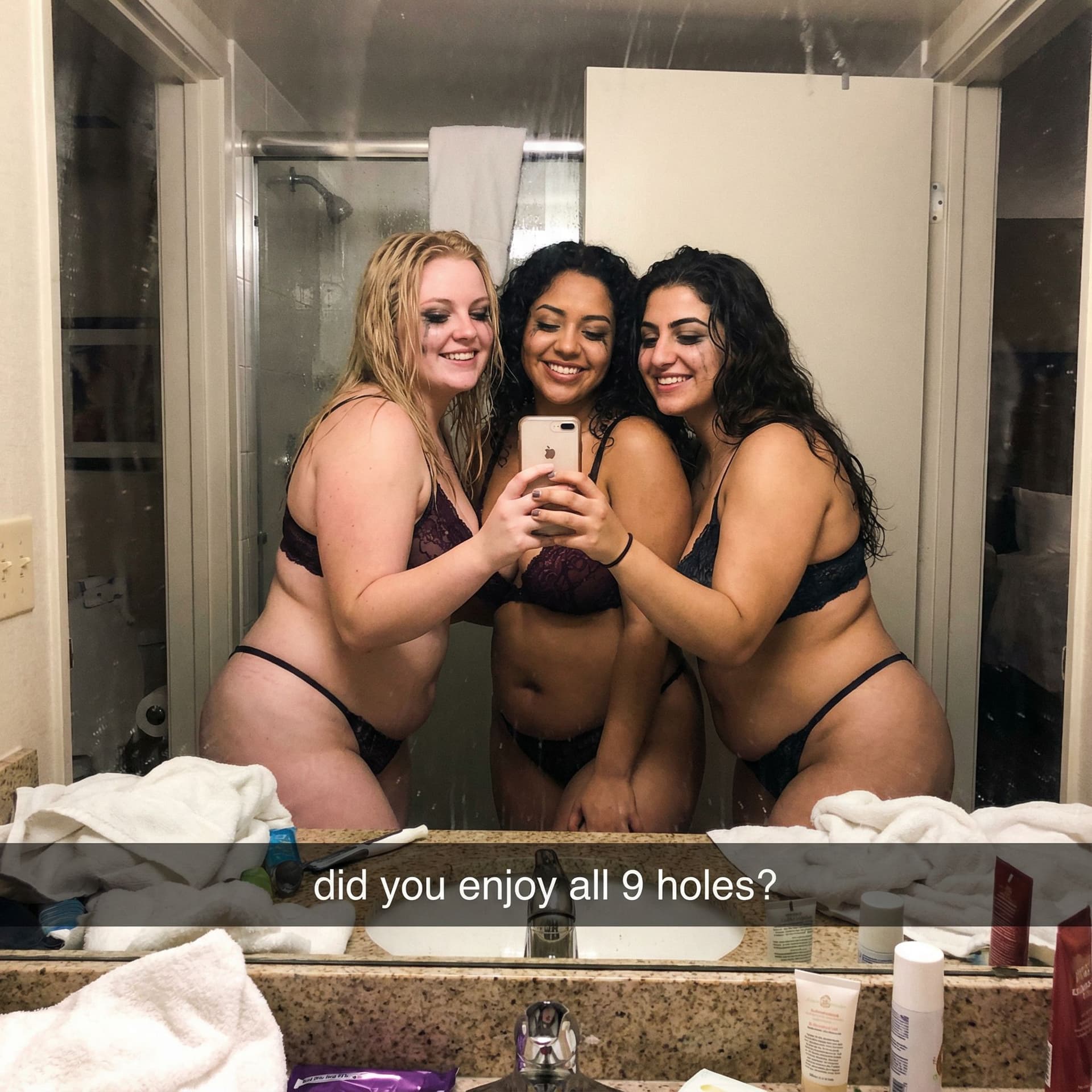 AI generated: 3 chubby 22 year old blonde women take a smiling mirror selfie in a messy hotel bathroom. They are w...