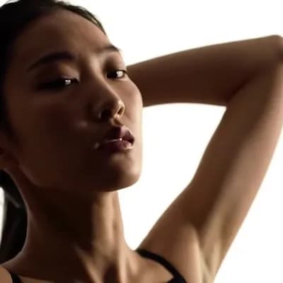 AI generated video: Arms raised, hands behind head. Pursed lips. 