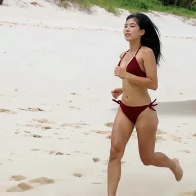 AI generated video: asian lady in her bikini running down a white sand beach with sweat glistening on her skin