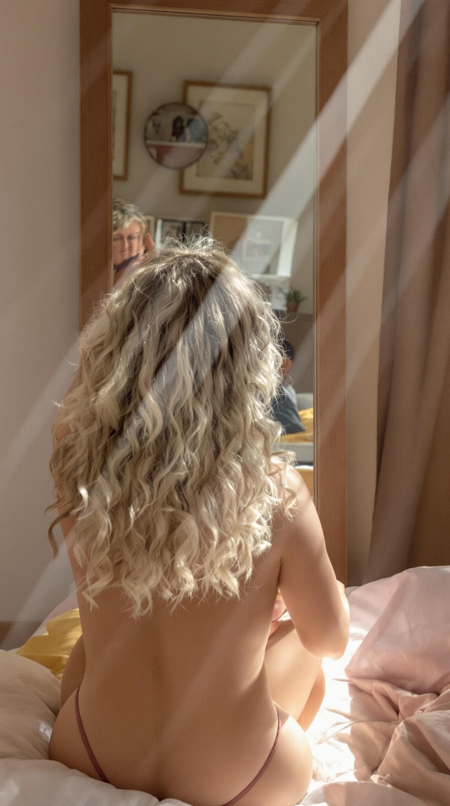 AI generated: Beautiful Italian woman with blonde curly hair sitting on her bed and taking off her bra in front of...
