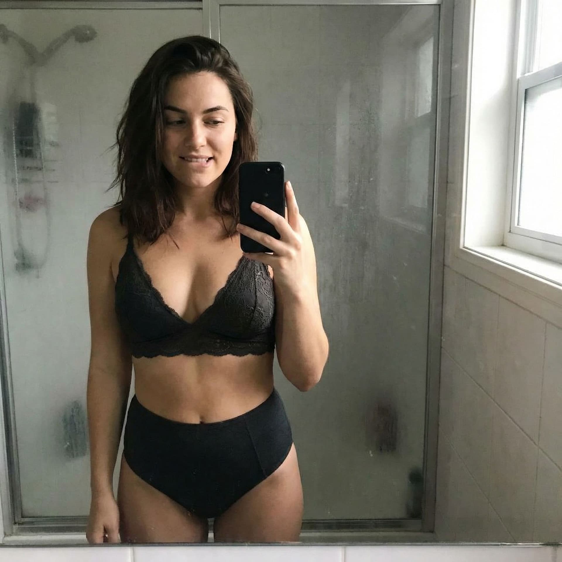 AI generated: Casual mirror selfie in a bathroom, smartphone photo quality. Slim brunette adult with a playful exp...