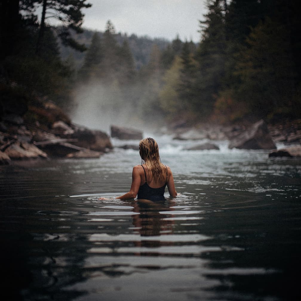 AI generated: hot spring in a river flow, steam rises from the water, a woman with long wet blonde hair swims in t...