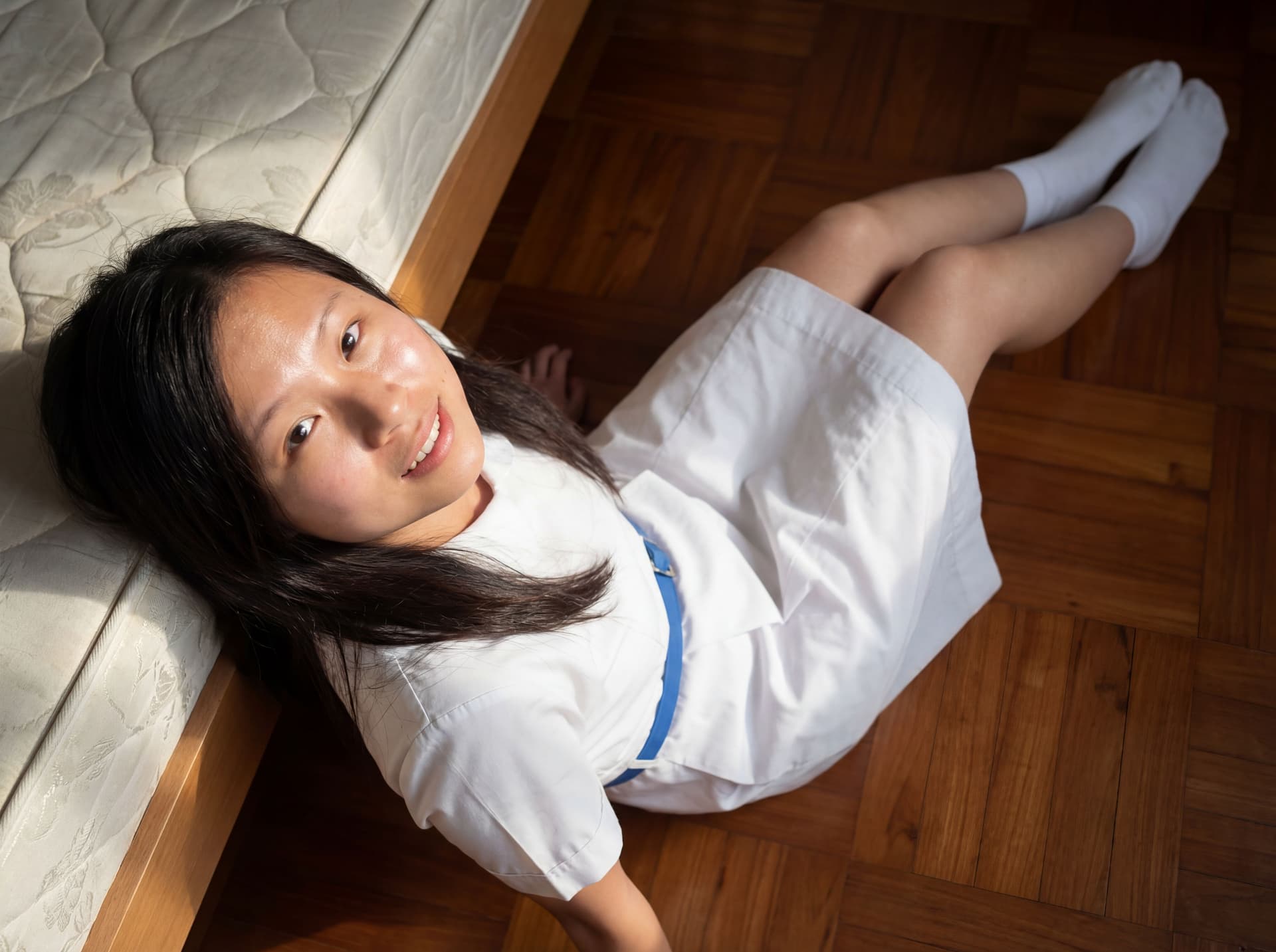 AI generated: the lady with hong kong uniform lies on floor beside a bed, put her legs on bed. uniform is white wi...