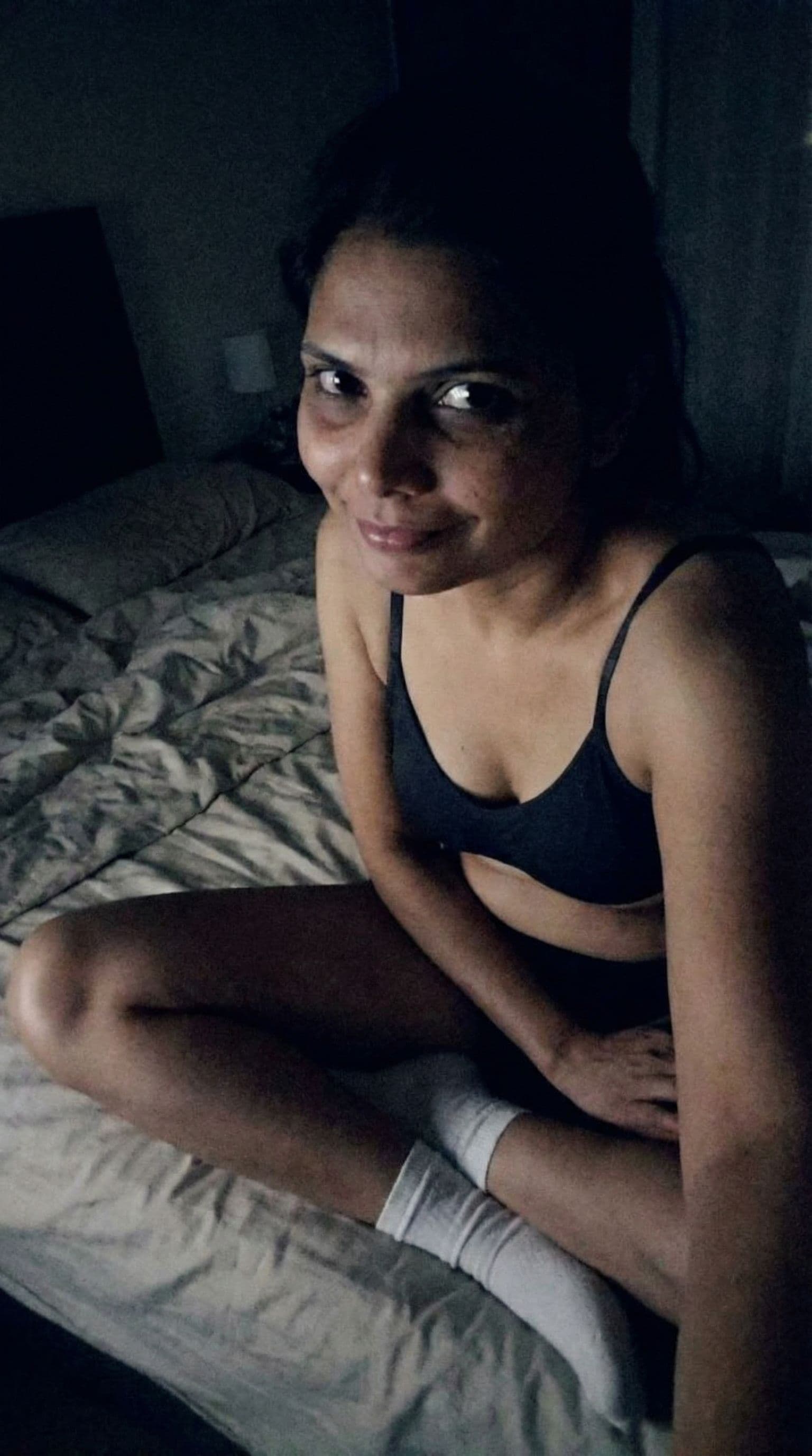 AI generated: Seductive face, selfie looking at me,a sloppy snapshot. Sitting on a bed at night teasing(no lights)...