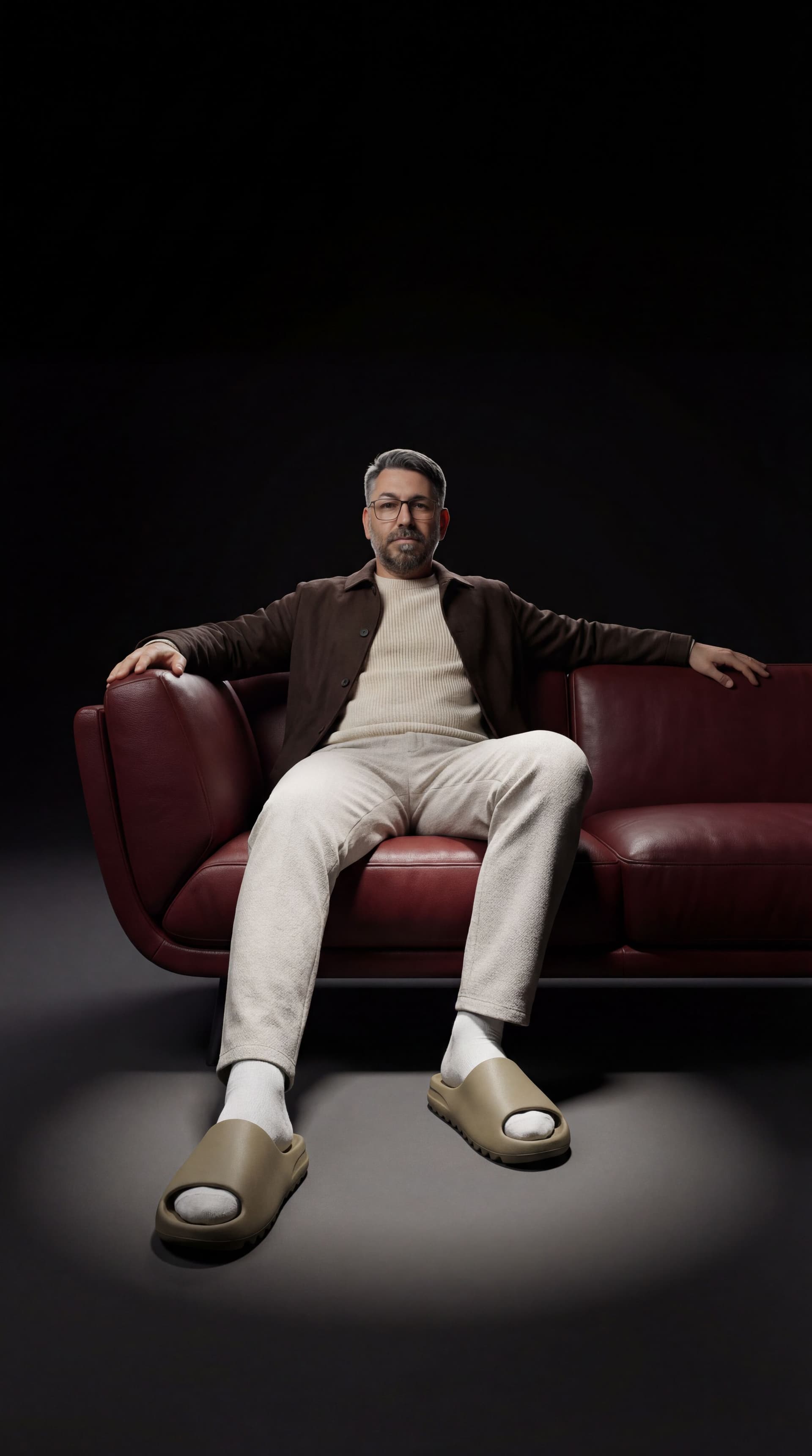 AI generated: A minimal, high-end studio portrait of one person sitting on a dark red curved modern leather sofa. ...