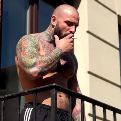 AI generated video: Un homme musclé et tatoué, torse nu, se tient sur un balcon. Il est chauve avec une barbe épaisse et...
