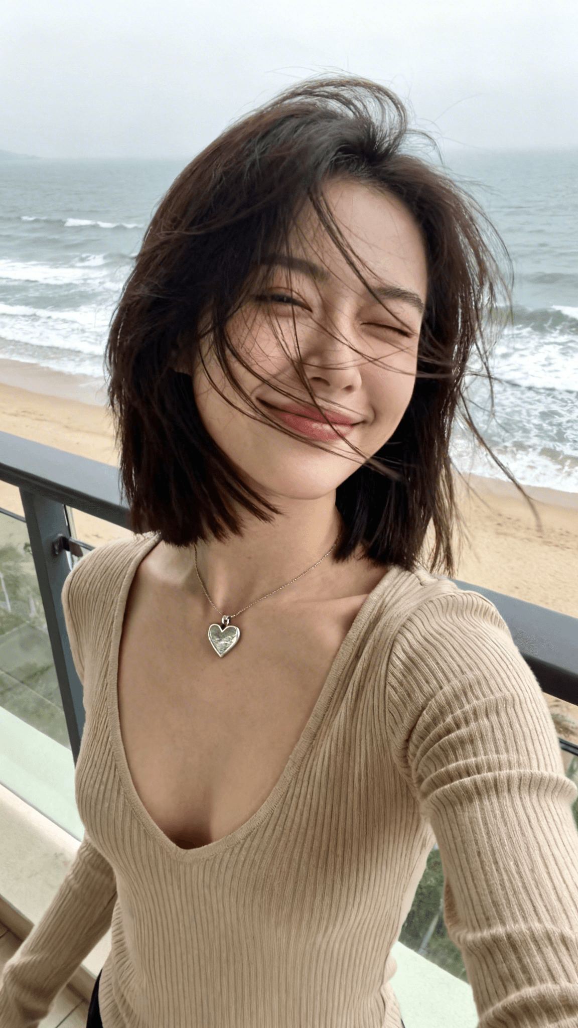 AI generated: { "subject": { "description": "A young Asian woman taking a high-angle selfie on a seaside balcony, ...