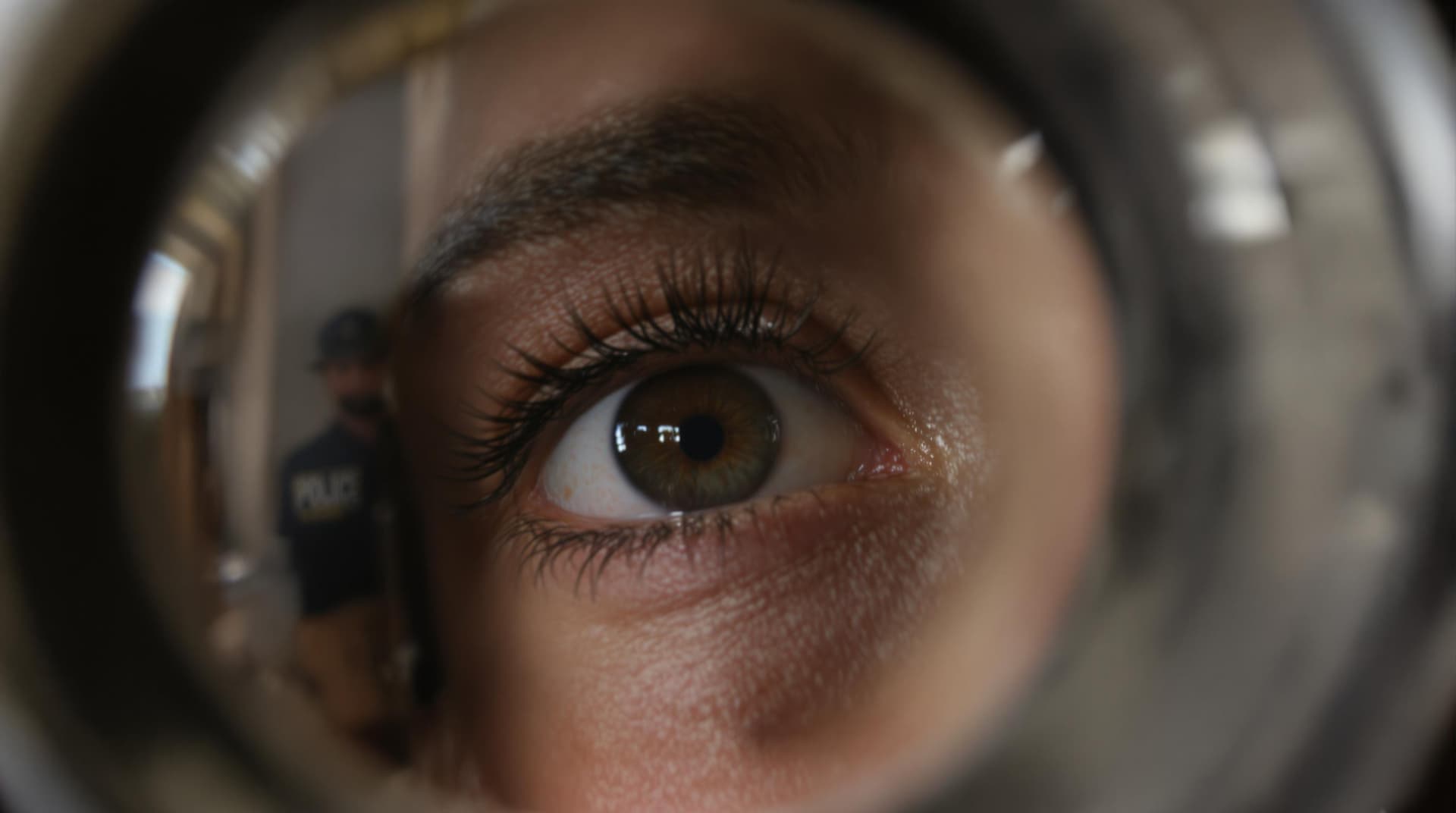 AI generated: Close-up of the woman’s eye looking through a peephole. An uncomfortable police officer stands outsi...