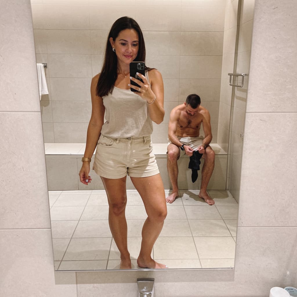 AI generated: The image appears to be a mirror selfie taken in a bathroom or dressing area with tiled floors and w...