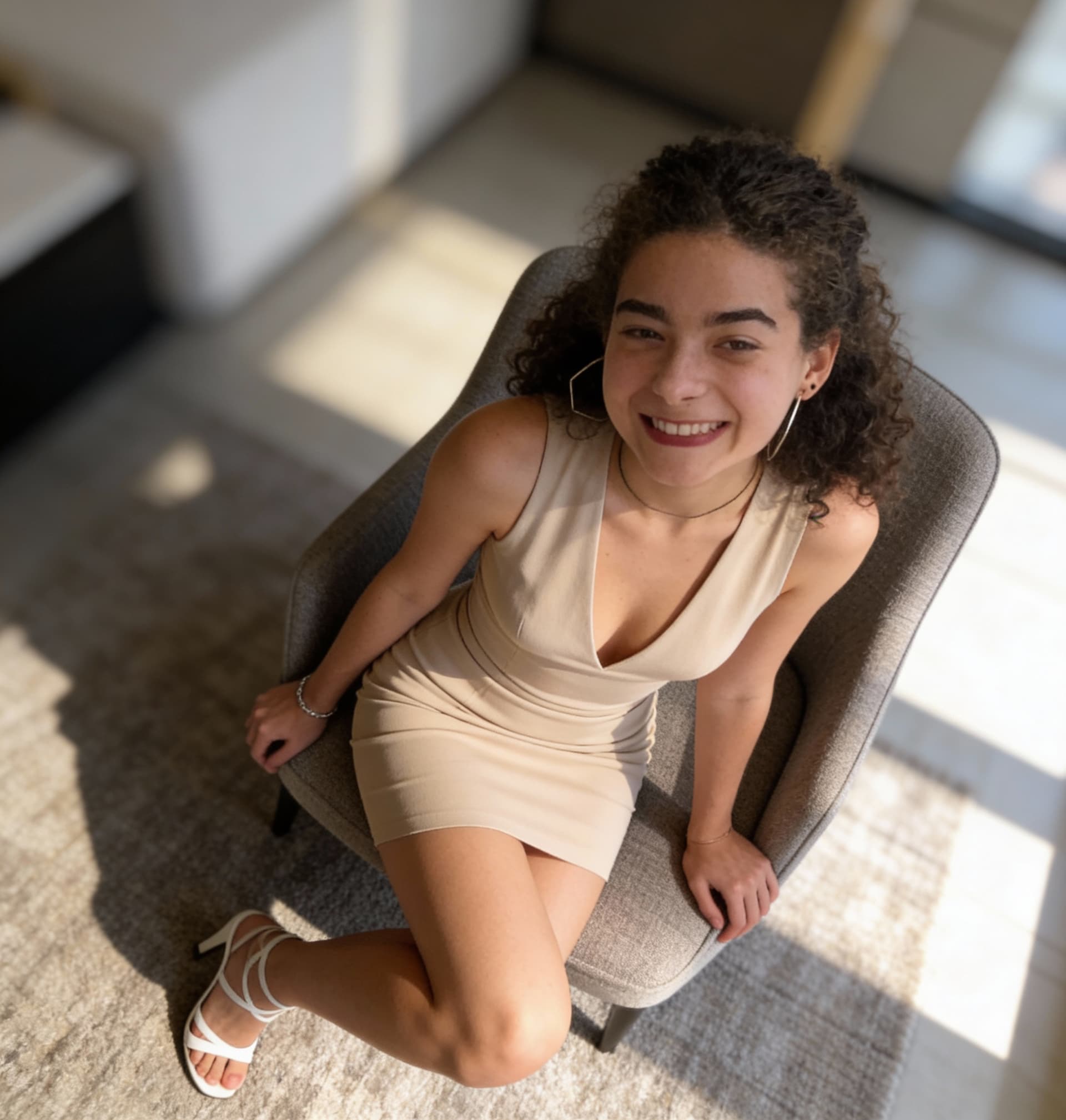 AI generated: warm, inviting smile. She wears a form-fitting, sleeveless beige mini-dress with a deep V-neckline, ...