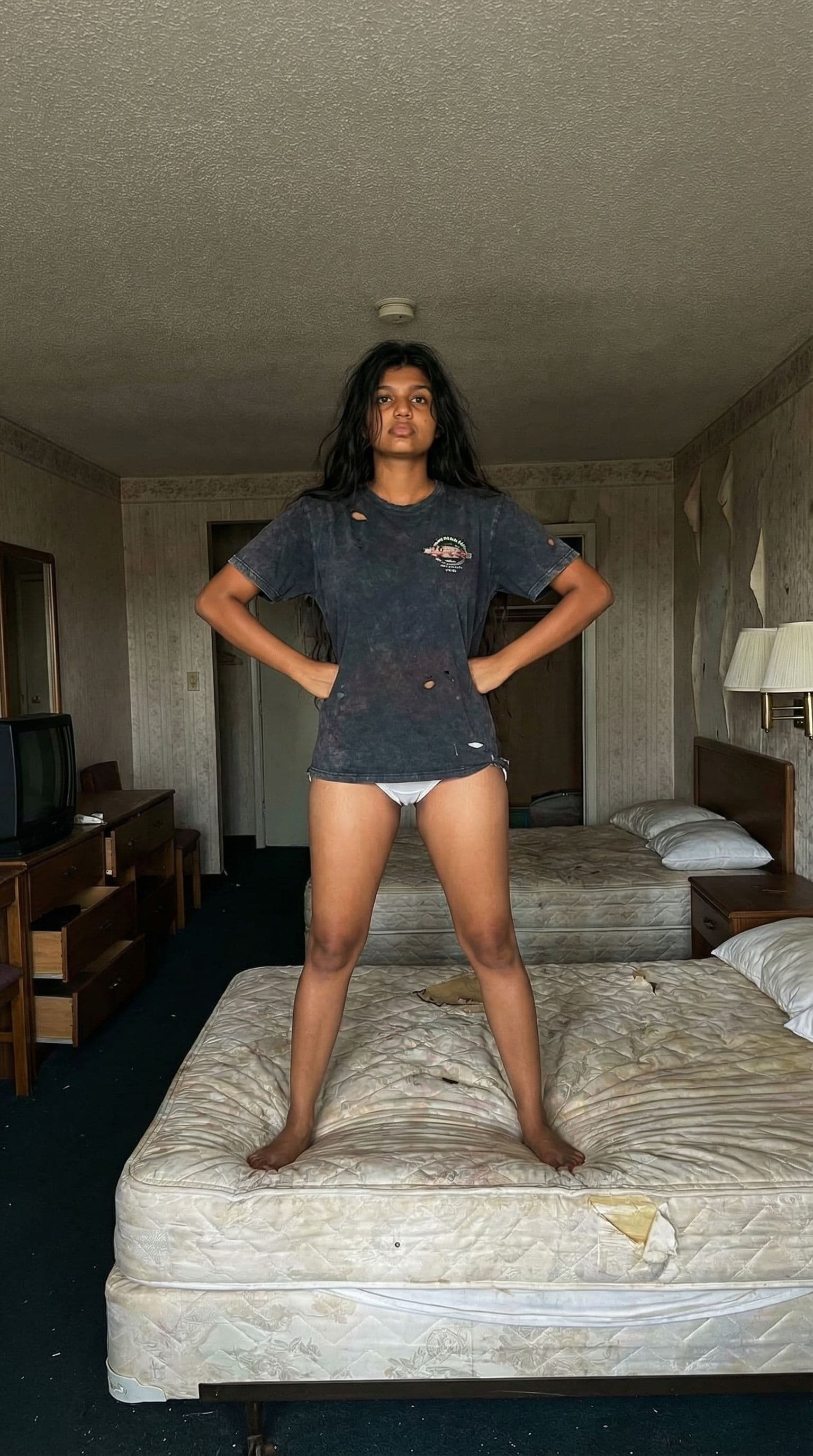AI generated: In a very cheap looking motel room. One beautiful brunette girl with a tan and brown eyes is standin...