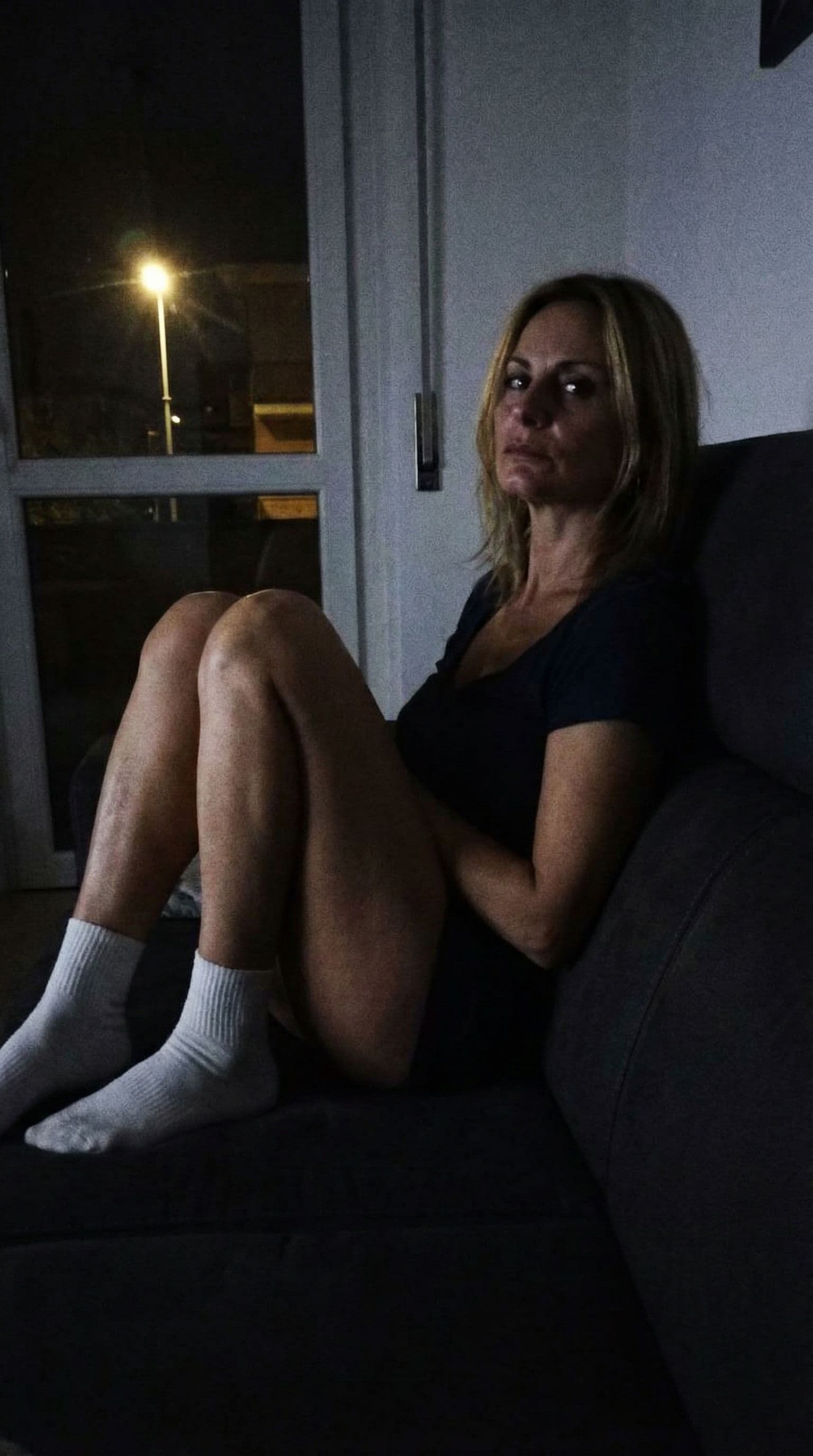 AI generated: Sexy looking at me,a sloppy snapshot. Sitting on a couch at night(no lights), wearing a mini top and...