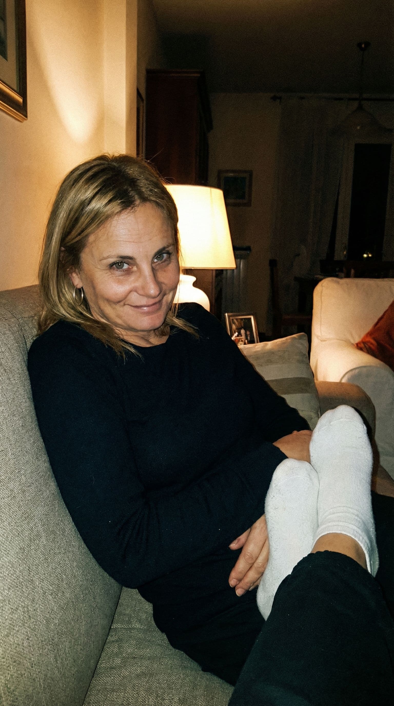 AI generated: looking at me,a sloppy snapshot. Sitting on a couch at night teasing, home mini top and white socks