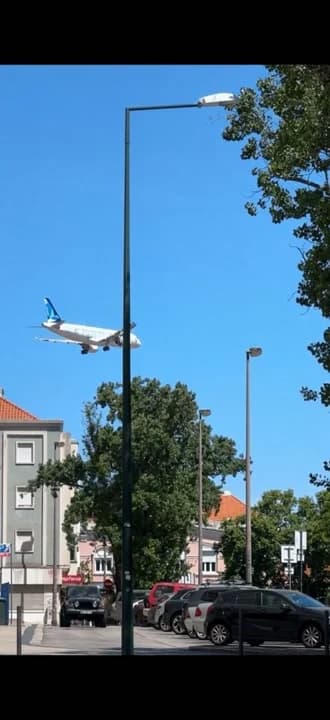 AI generated video: Static camera, Lisbon street, empty sky at start, 
white commercial airplane with blue tail enters 
...