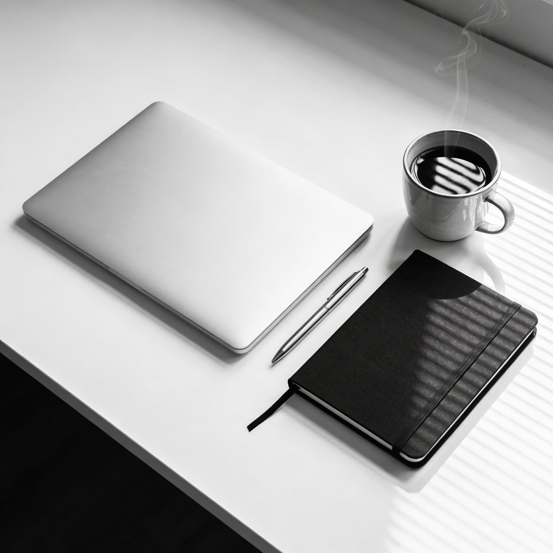 AI generated: High-angle flat lay of a minimalist white desk, featuring a sleek silver laptop, a black moleskin no...