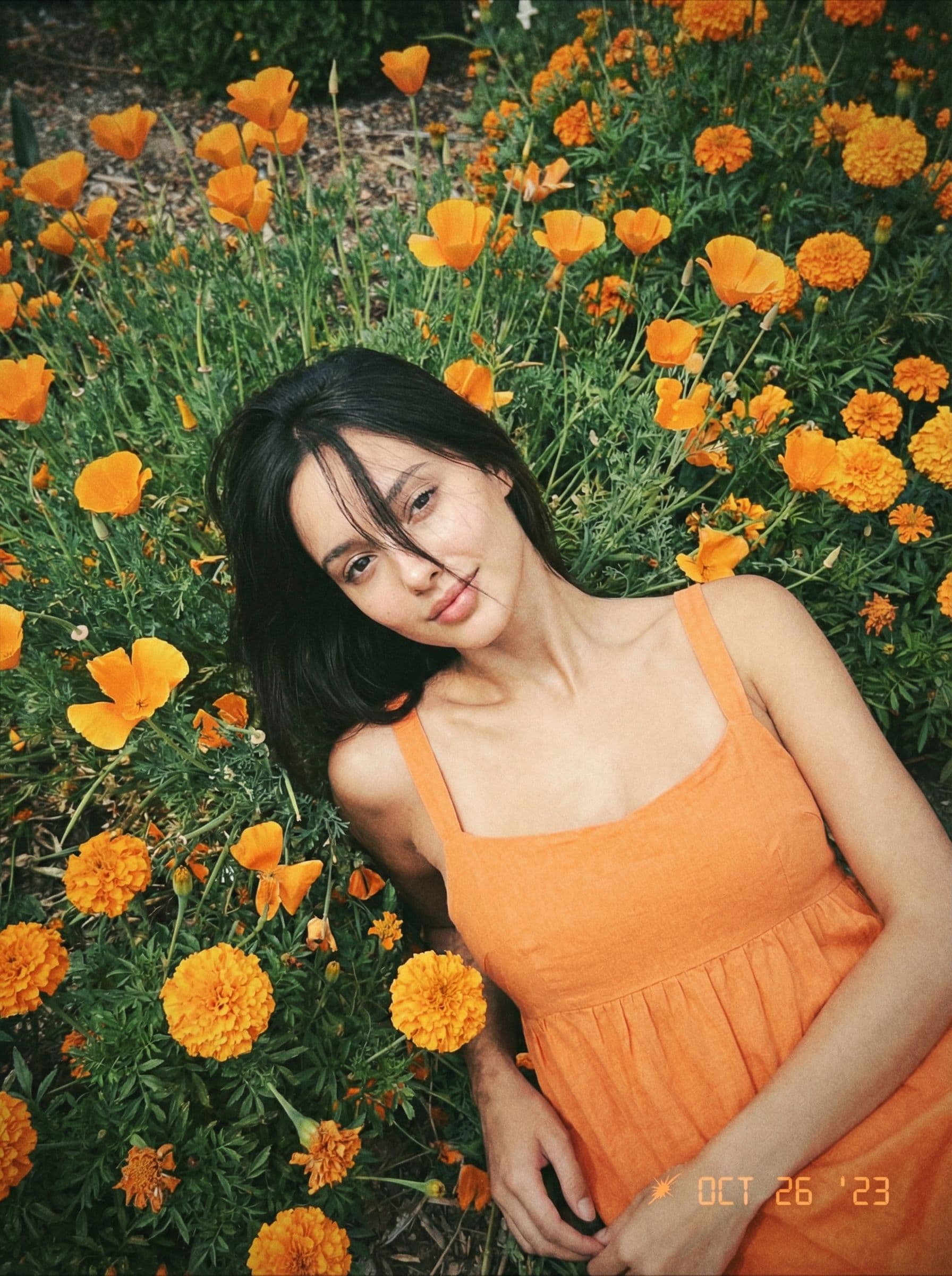 AI generated: Kodak disposable photography of beautiful fashion model with orange dress, laying on orange flower b...