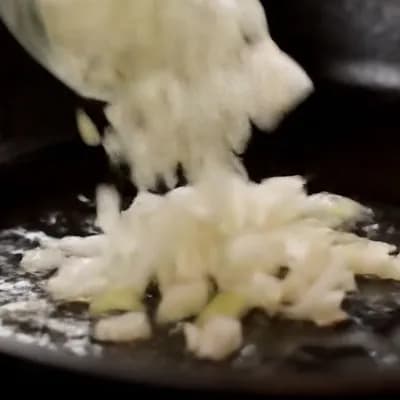 AI generated video: A close up in a smooth, slow pan focuses intently on diced onions hitting a scorching hot pan, insta...