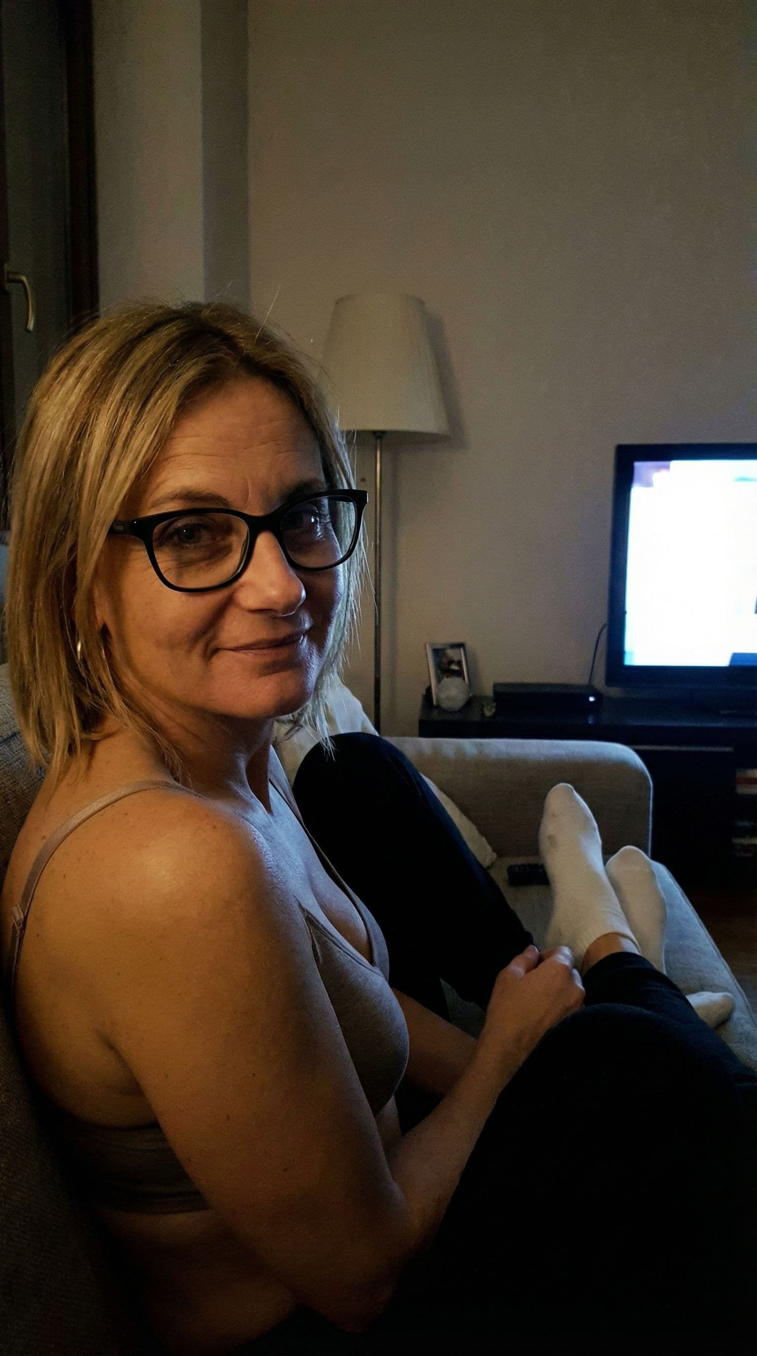 AI generated: looking at me,a sloppy snapshot. Sitting on a couch at night teasing, home bra and white socks, glas...