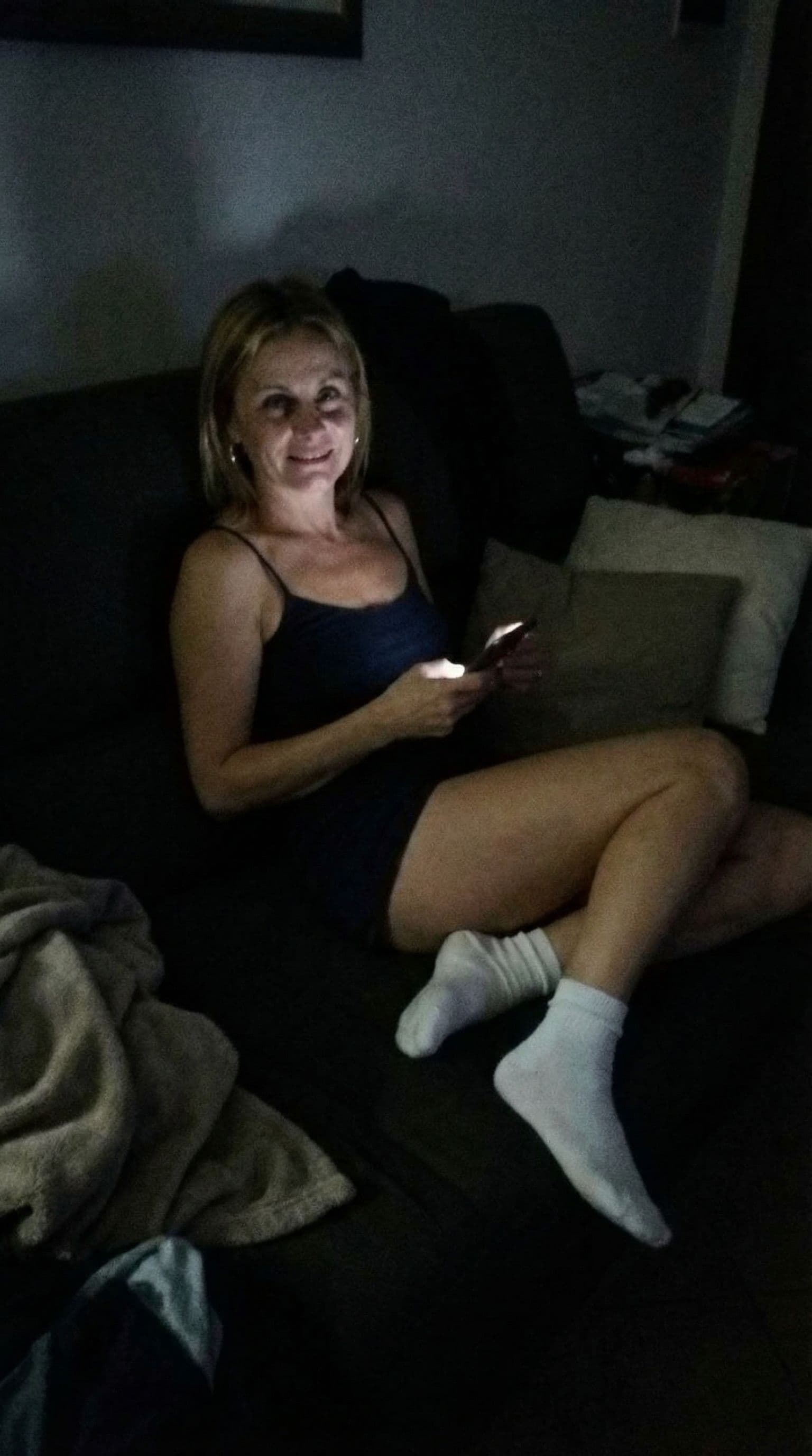 AI generated: looking at me,a sloppy snapshot. Sitting on a couch at night(no lights), wearing a mini top and whit...