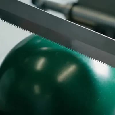 AI generated video: Close-up shot of an ultra-sharp industrial knife or saw slowly cutting through a glossy green bowlin...