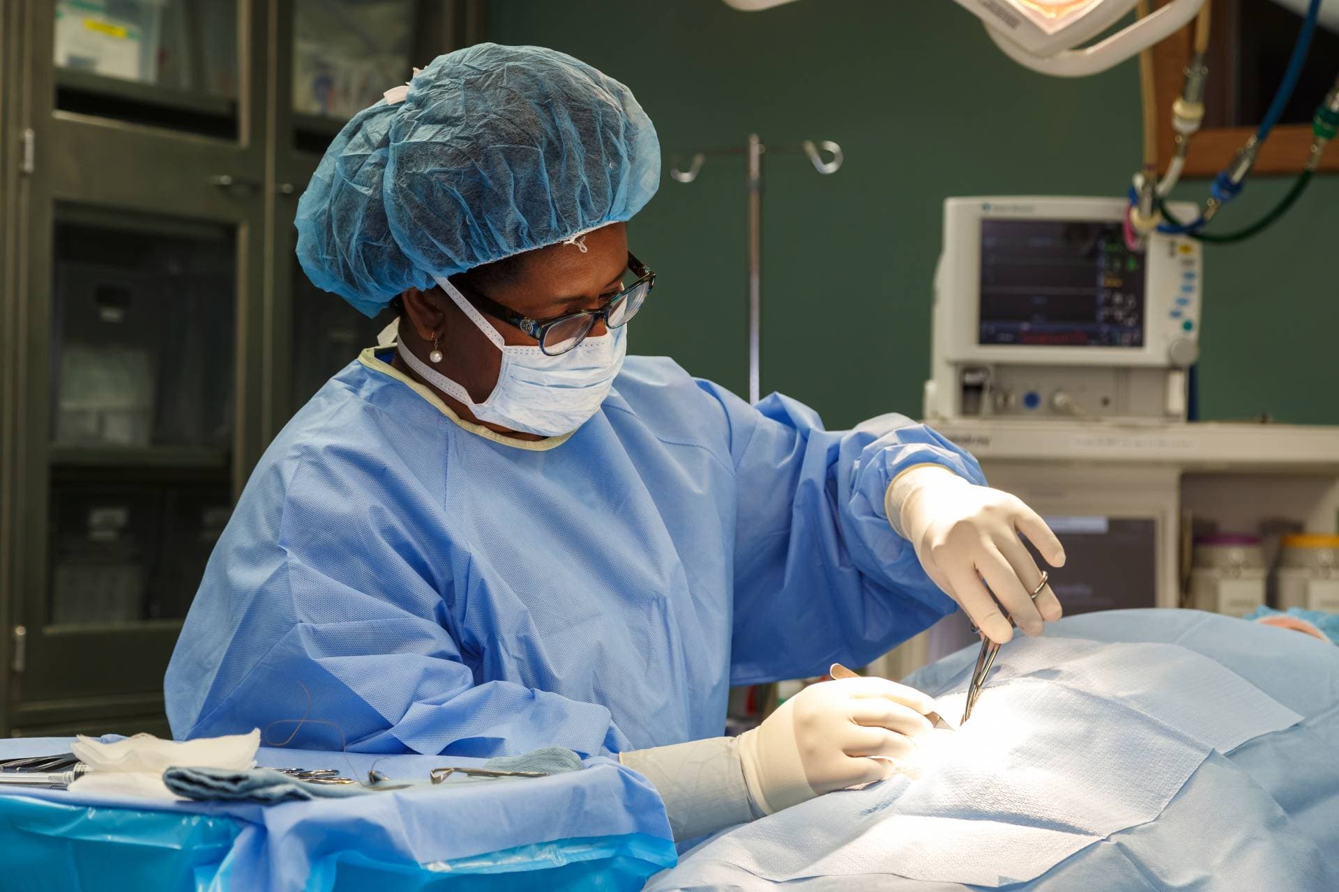 AI generated: A female surgeon in a blue surgical gown, white surgical, white surgical mask and teal latex gloves ...