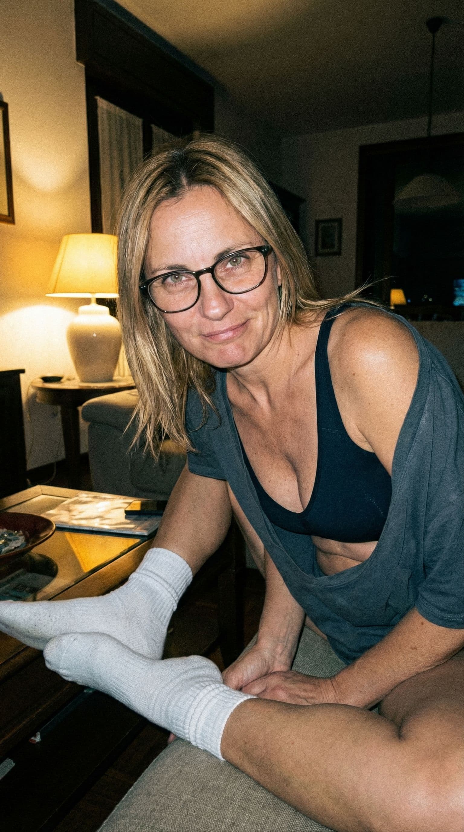 AI generated: looking at me,a sloppy snapshot. Sitting on a couch at night teasing, home bra and white socks, glas...