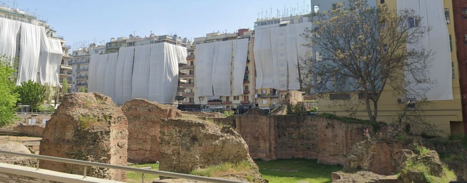 AI generated: Cover the buildings surrounding the ancient ruins with white curtains.