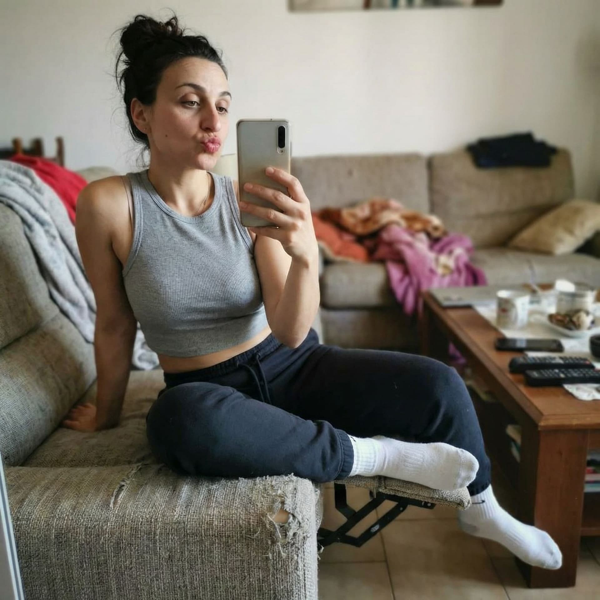 AI generated: Takes a selfie while sitting on a couch, sticking lips, wearing a cropped tanktop and white socks, s...