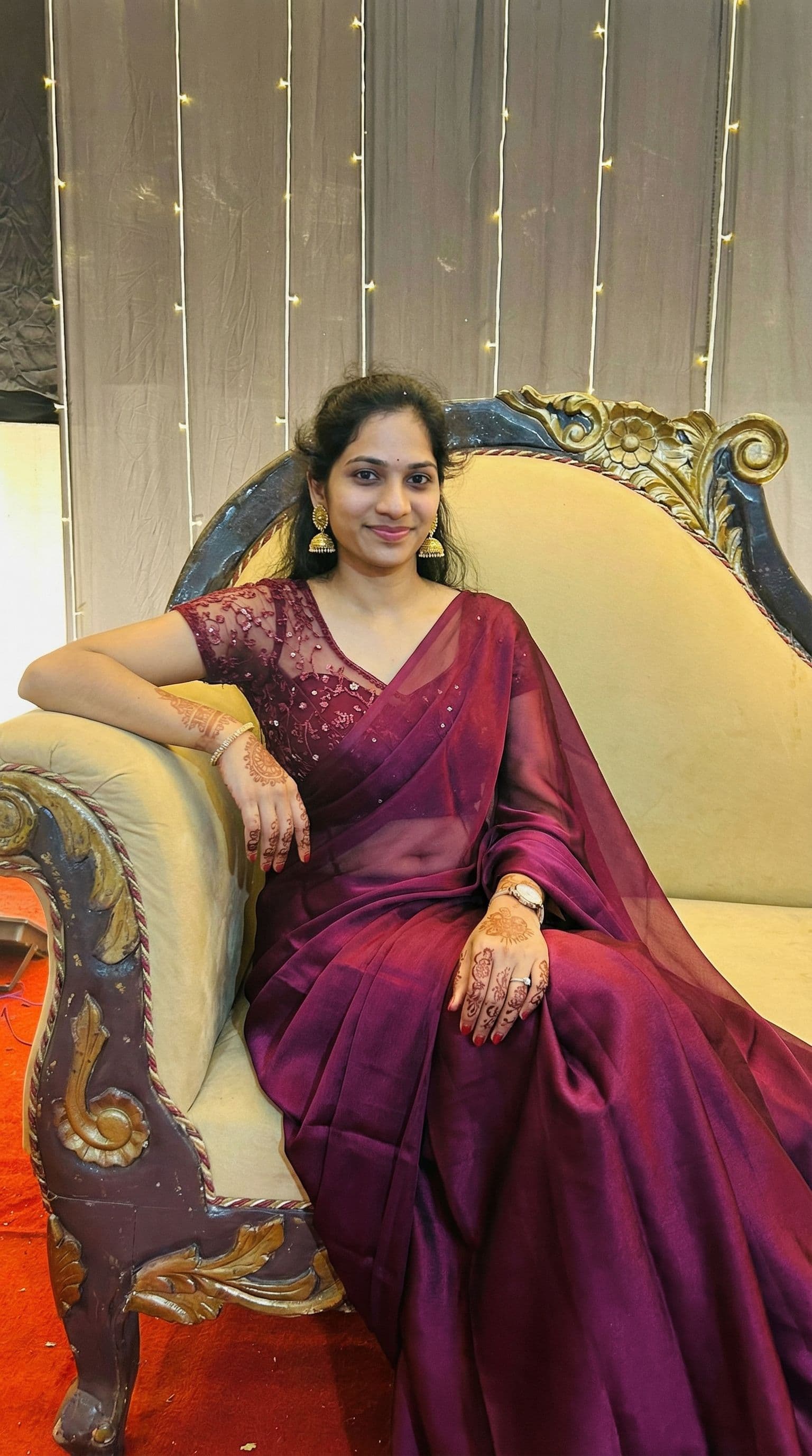 AI generated: Edit the uploaded image of the woman sitting on an ornate sofa. Replace her outfit with an elegant a...
