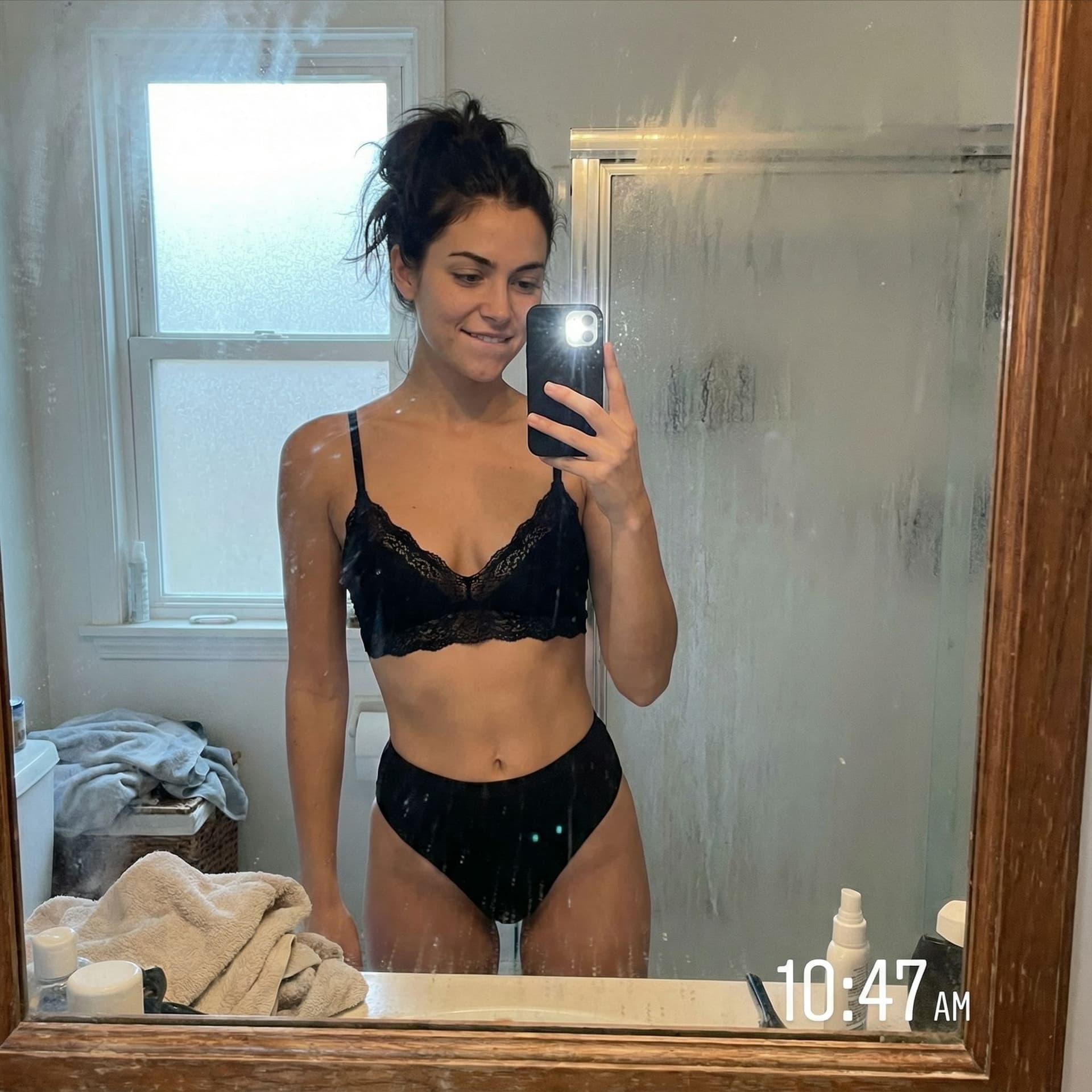 AI generated: Casual mirror selfie in a bathroom, smartphone photo quality. Slim brunette adult with a playful exp...