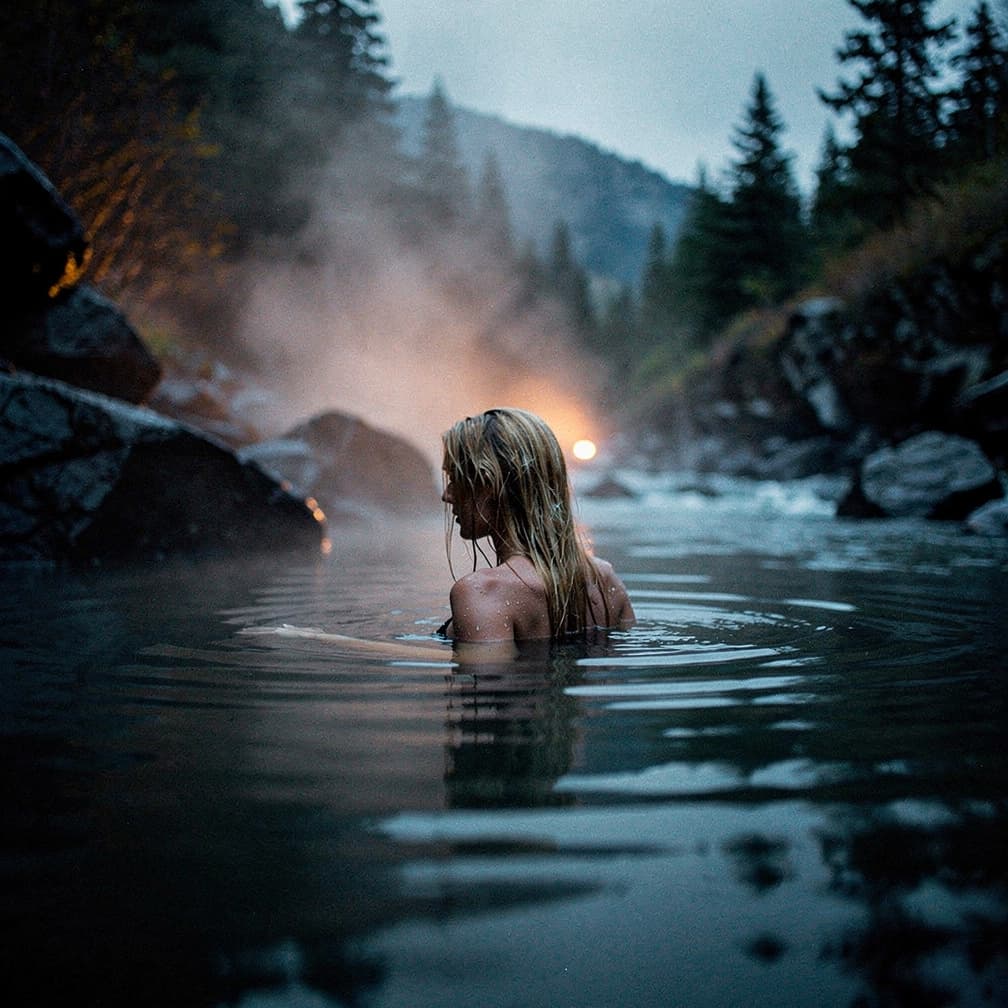AI generated: hot spring in a river flow, steam rises from the water, a woman with long wet blonde hair swims in t...
