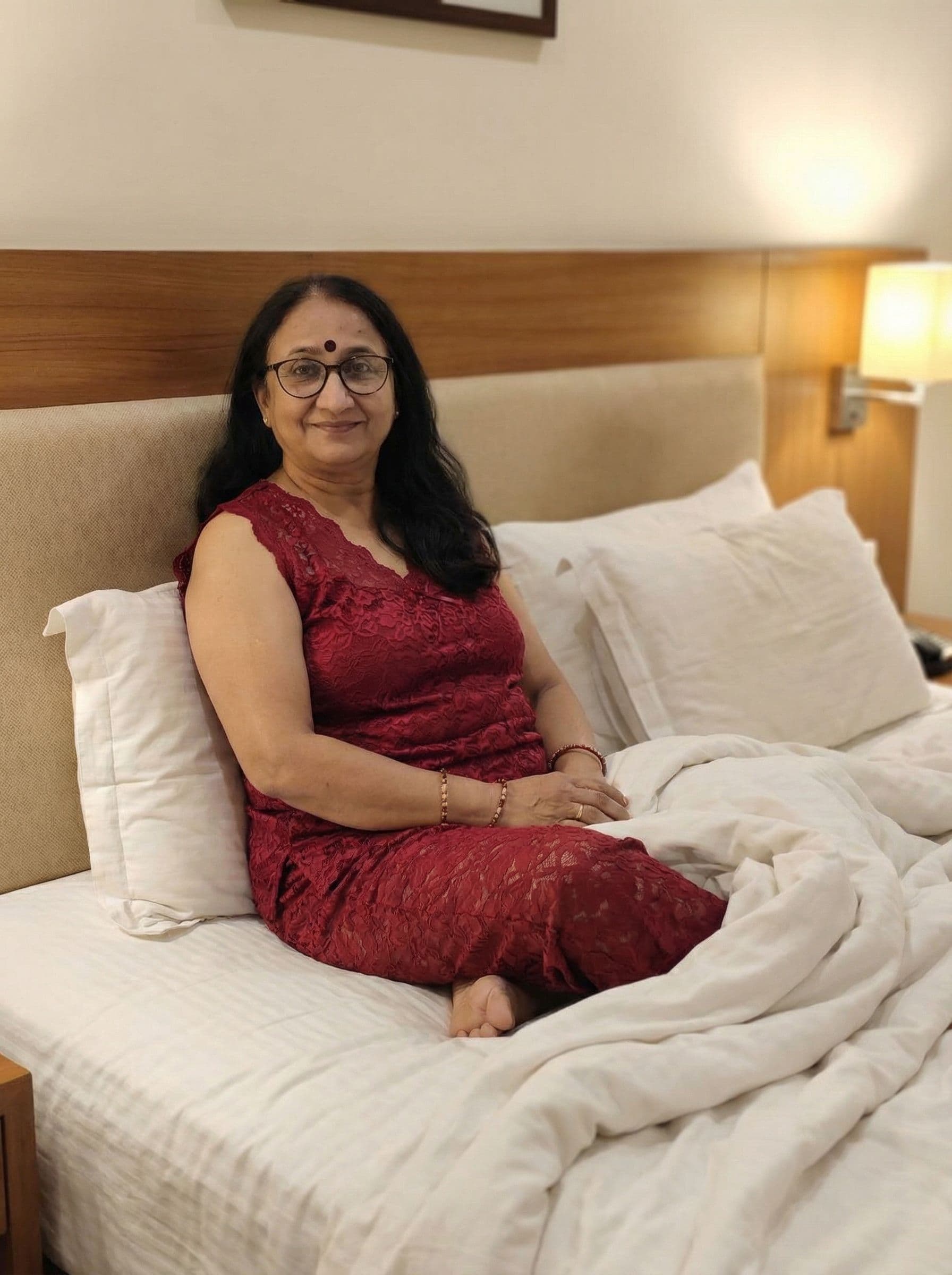 AI generated: Indian women of age 40 years old.wearing two peace deep red lace sleeveless night suit.sitting on be...