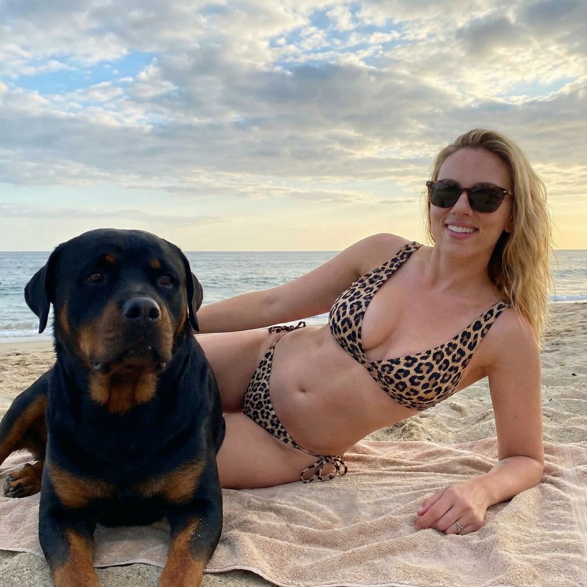 AI generated: Scarlett Johansson with leopard bikini at the beach, lying on side at the beach with her rottweiler,...