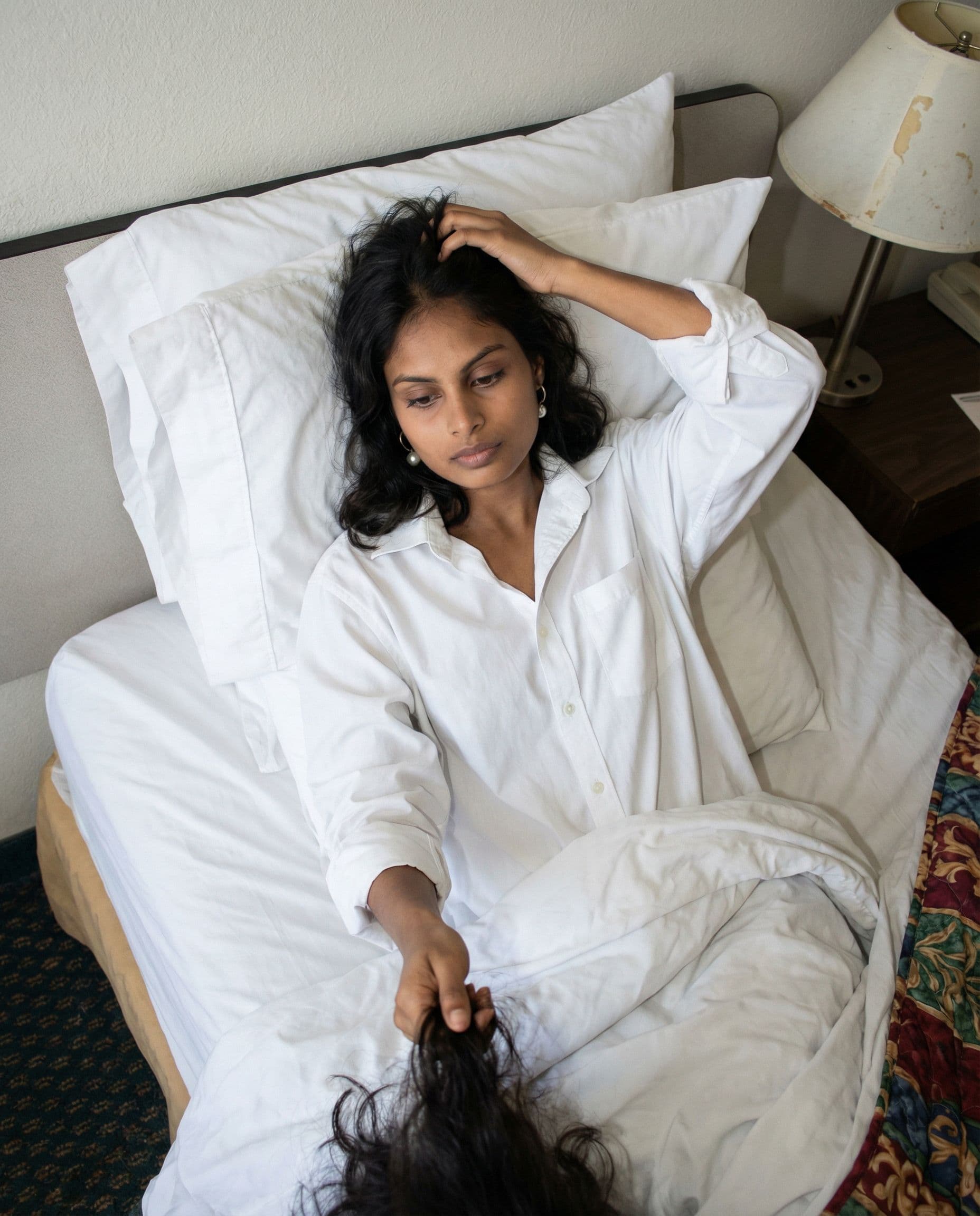 AI generated: .....Scene: Inside a modest motel room, on the bed amid rumpled white sheets. She lies back against ...