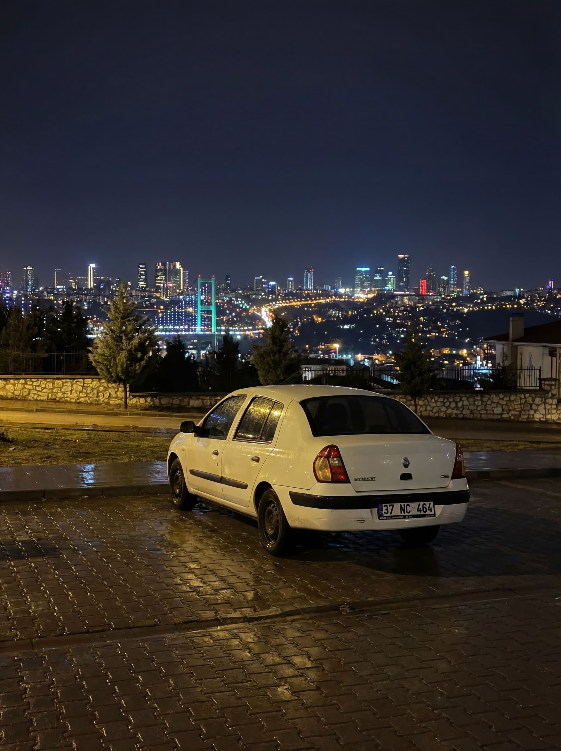 AI generated: Araba ıslak, yerler ıslak. Arkada muazzam ve hoş bir gece manzarası beni bekliyor