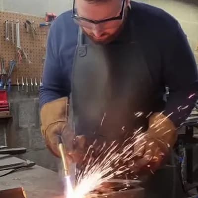 AI generated video: A realistic smartphone video of a man welding metal with a blowtorch in a small workshop. He’s weari...