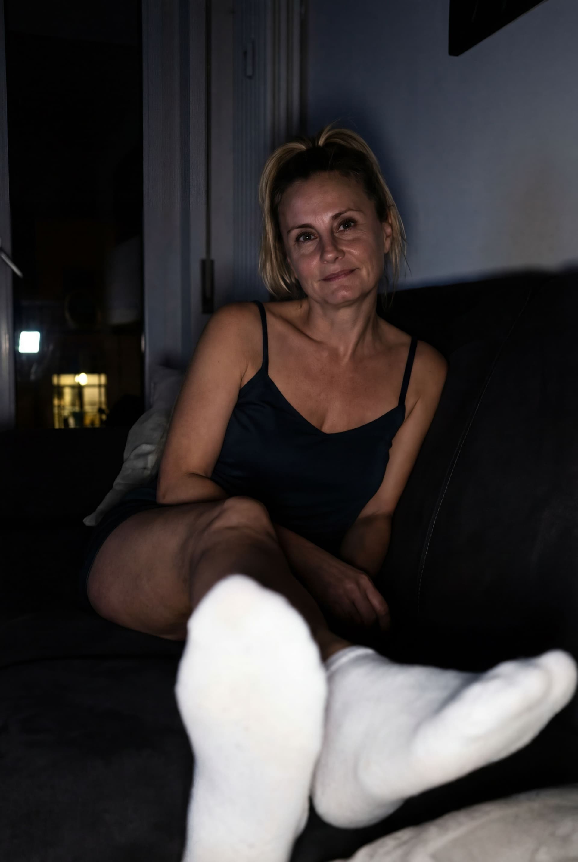 AI generated:  looking at me,a sloppy snapshot. Sitting on a couch at night(no lights), wearing a mini top and whi...
