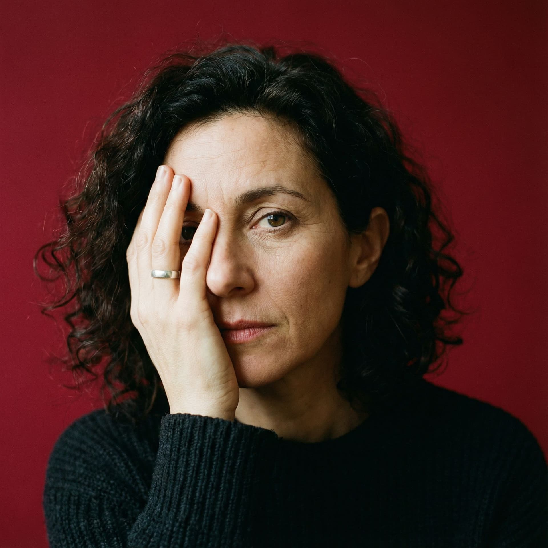 AI generated: image of a woman with a thoughtful expression, covering half of her face with her hand, pure red bac...