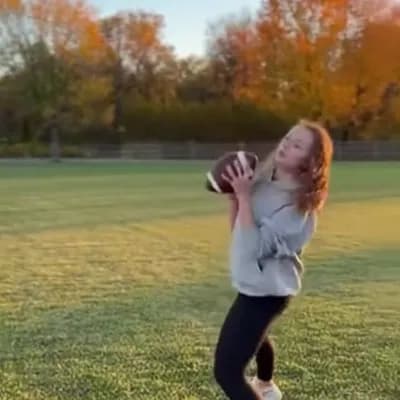 AI generated video: She stands up and catches a football, she turns around and kickes it back 