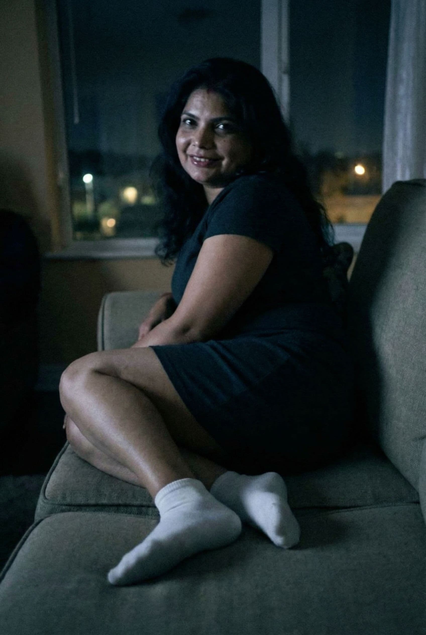 AI generated:  looking at me,a sloppy snapshot. Sitting on a couch at night teasing(no lights), wearing a mini dre...