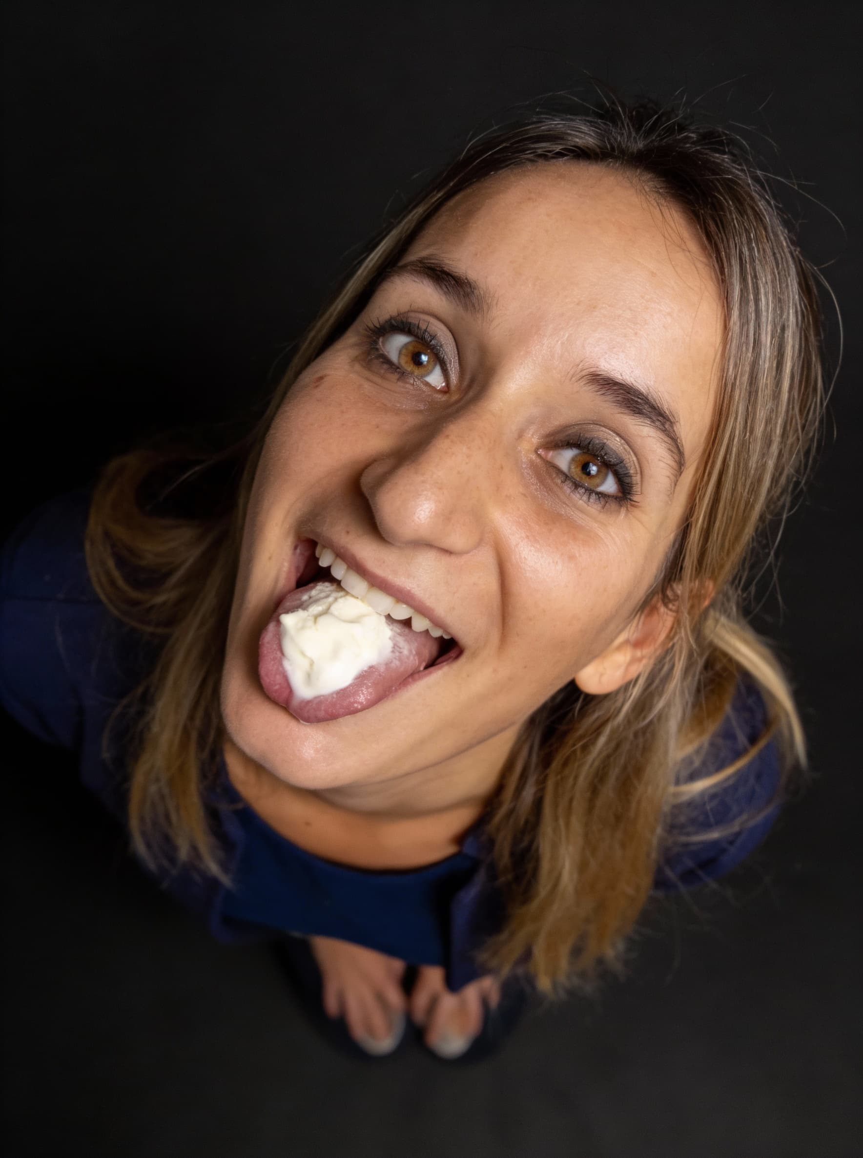 AI generated: selfie taken from a high overhead angle. kneels low, tilting her head back playfully with her tongue...