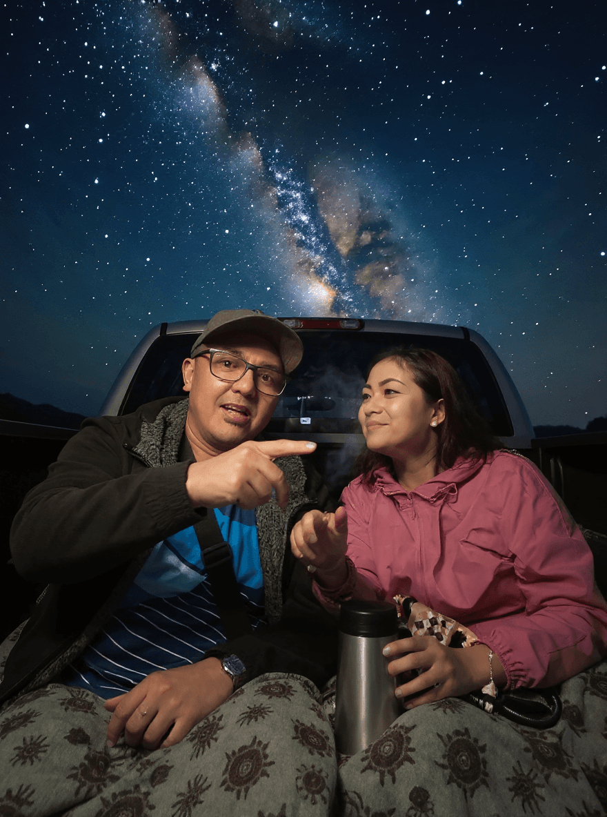 AI generated: A photorealistic scene of a couple in their early 40s sitting on the tailgate of a truck under a vas...