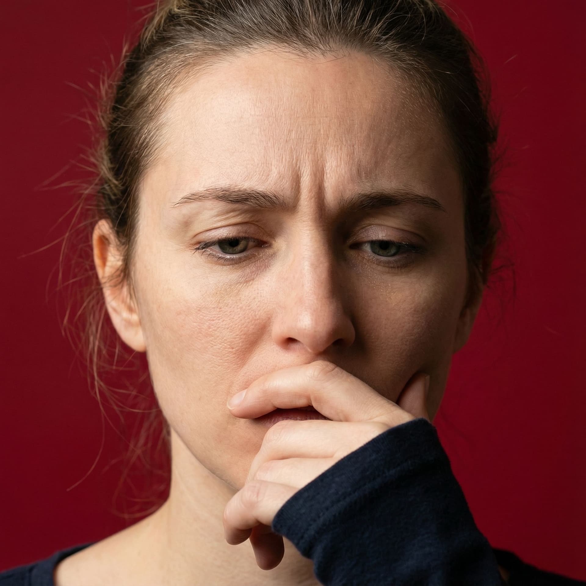 AI generated: image of a woman with a thoughtful expression, covering half of her face with her hand, pure red bac...