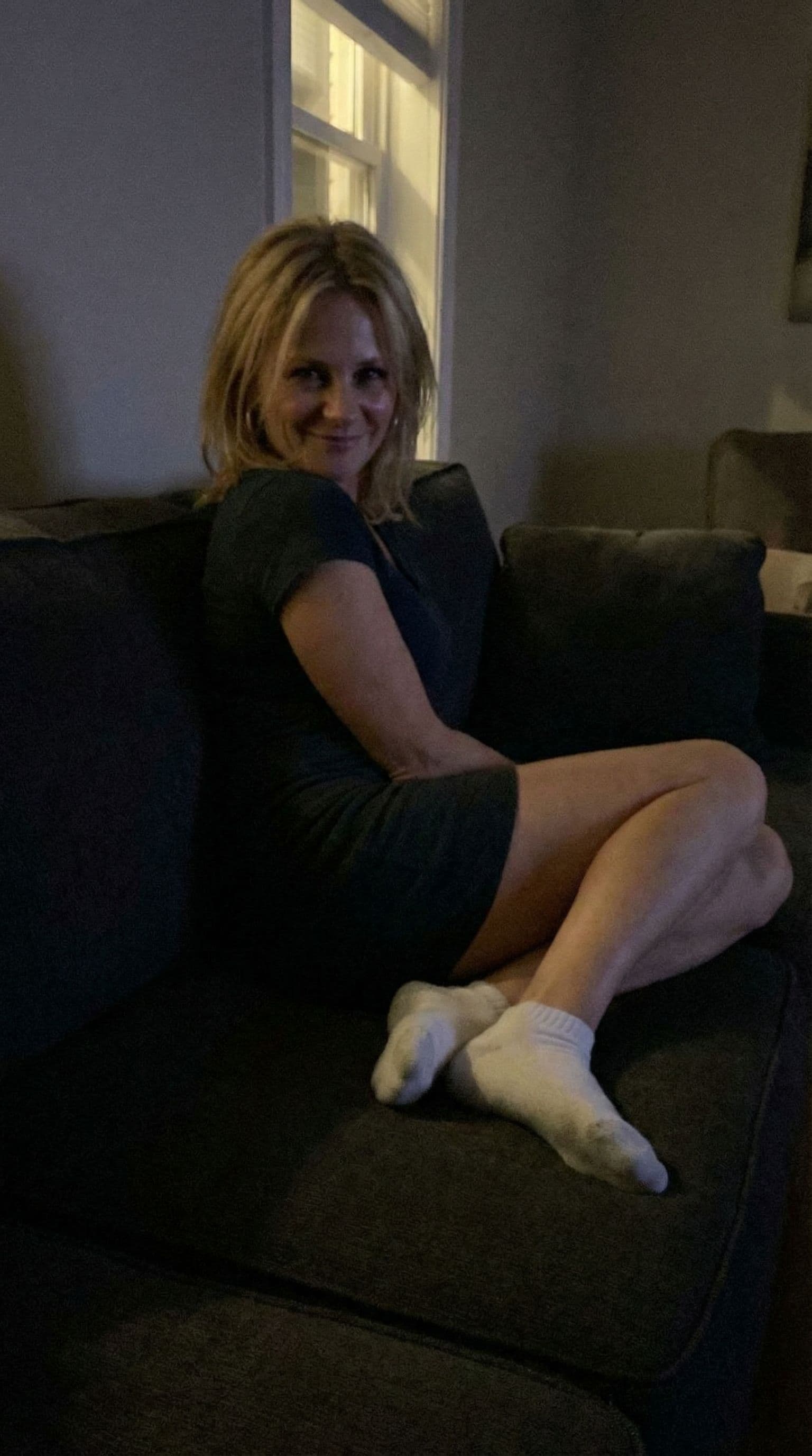 AI generated:  looking at me,a sloppy snapshot. Sitting on a couch at night teasing(no lights), wearing a mini dre...