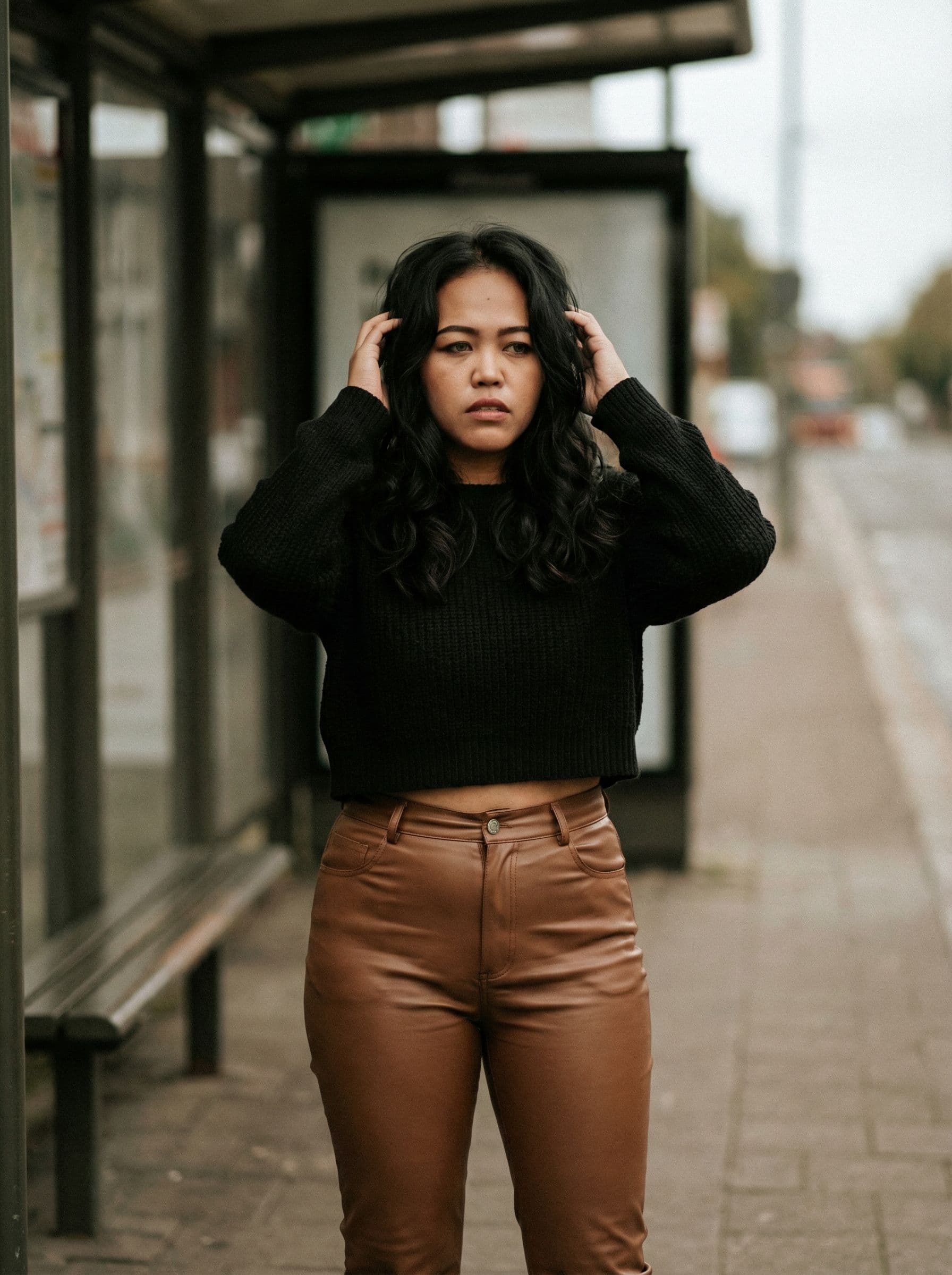 AI generated: a woman wearing a cropped top and leather super tight pants standing in front of the bus stop, effec...