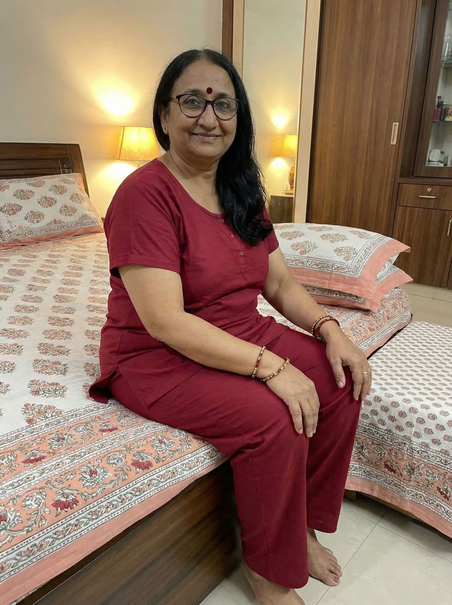 AI generated: Indian women of age 40 years old.wearing deep two peace night suit of red color.sitting on bed 